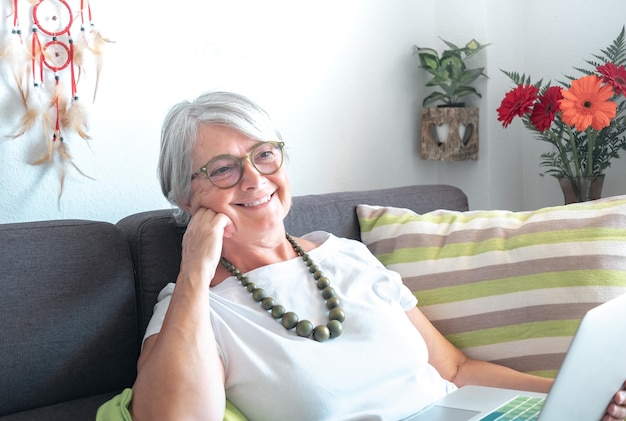 Senior relaxed woman smiling sitting on sofa using laptop grandmother enjoying new technology browsing on internet concepts about communication online ecommerce