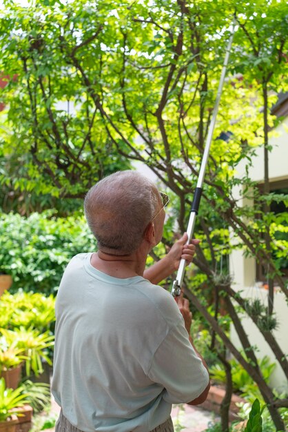 Photo senior retired asian man pruning tree in home backyard during free time