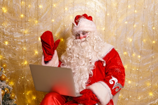 Babbo natale senior in costume tradizionale rosso che chatta online sul laptop durante la videochiamata nel periodo natalizio...