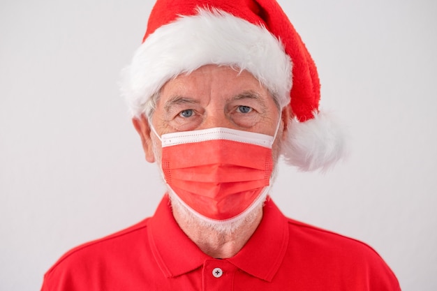 Senior serious man dressed in red as santa claus wearing a red surgical mask due to coronavirus pandemic