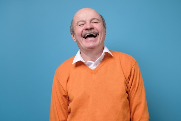 Senior Spaanse man in oranje trui lachen om grap