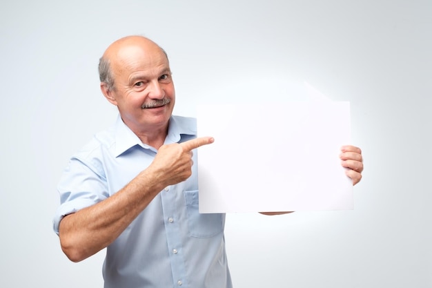 Senior Spaanse man met snor houdt het witte bord in een studio witte achtergrond