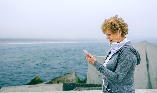 Photo senior sportswoman looking at her smartphone by sea pier