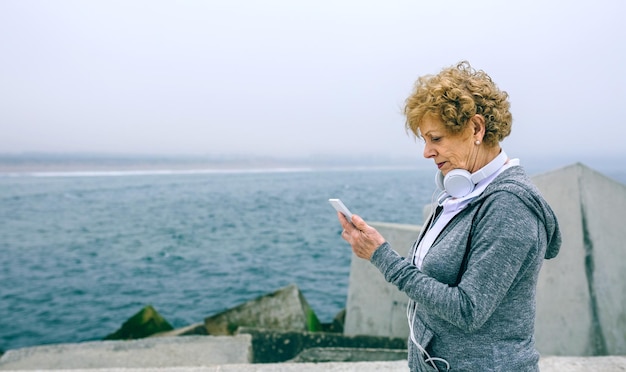 Senior sportvrouw kijkt naar haar smartphone bij de zeepier