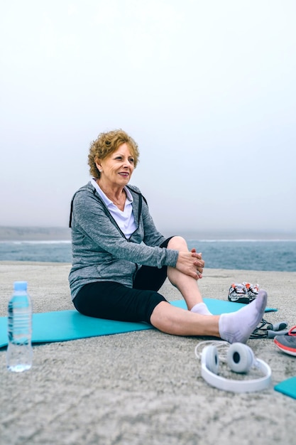 Senior sportvrouw ontspannen op yoga mat door zee pier