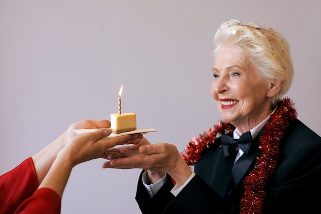 Senior stijlvolle vrouw in smoking blaast kaars op haar verjaardagstaart