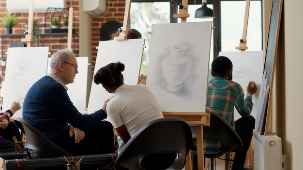 Senior student talking to young woman about drawing lesson, using pencil to create artwork sketch in art school. Inspiration program to draw vase model on canvas for personal growth.