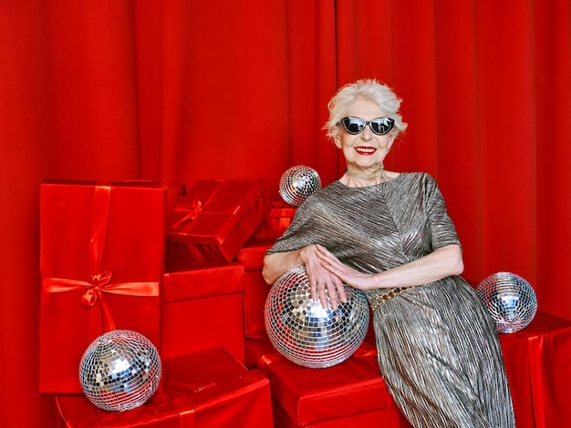 Senior stylish elegant woman with disco ball wine on red\
background. party, fashion, celebration, an