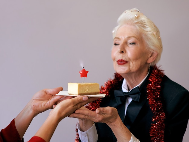 senior stylish woman in tuxedo blowing candle on her birthday cake