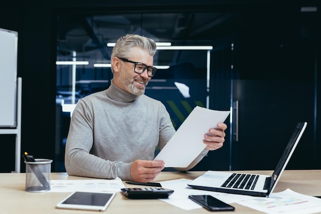 Senior successful businessman and investor working on paper work in the office mature gray haired