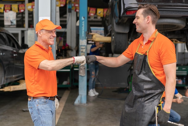 Photo senior technician bumps fist with worker man while working in garage auto service center