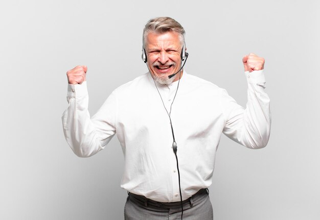 Senior telemarketer shouting aggressively with an angry expression or with fists clenched celebrating success