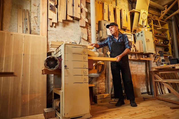 Senior timmerman in uniform werkt met een hout op een houtbewerkingsmachine bij de timmerfabriek