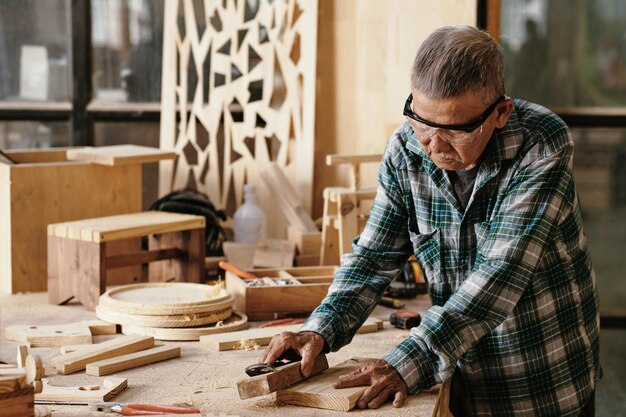 Senior timmerman polijsten klein bord met houten blok op zijn werkbank
