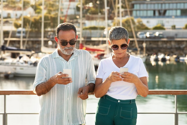 Senior toeristen paar met behulp van mobiele telefoons boeken zeecruise in de jachthaven