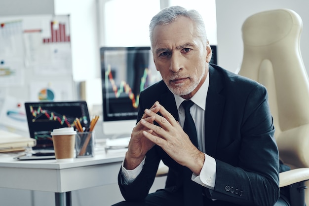 Senior trader in elegant business looking at camera while working at the office