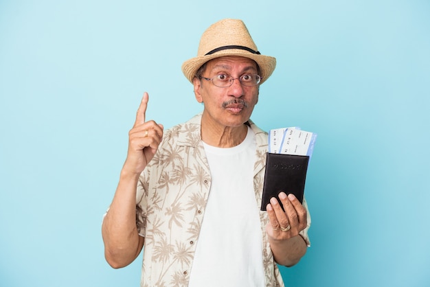 Senior traveler Indian middle aged man holding passport isolated on blue background having some great idea, concept of creativity.