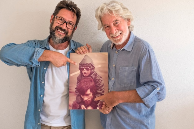 Senior vader en volwassen zoon in leeg appartement met verhuisdozen glimlachen met oude fotografie van beide toen ze veel jonger waren - concept van familie en liefde