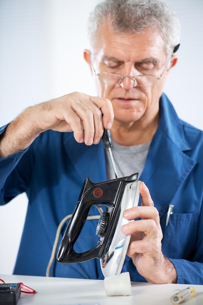 Senior volwassen elektricien die oud ijzer controleert en repareert.