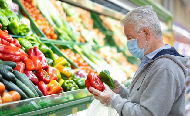 Senior volwassen man met chirurgisch masker als gevolg van coronavirus tijdens het winkelen in de supermarkt.