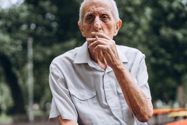 Senior volwassen mannen roken sigaret buiten in het stadspark wanneer ze op de bank zitten.