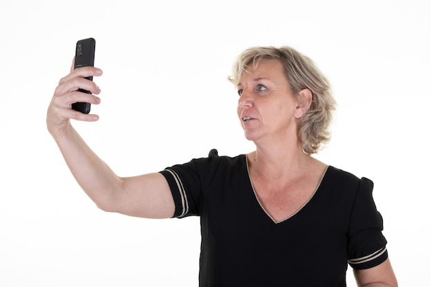 Senior vrolijke vrouw blond over geïsoleerde witte achtergrond maken mobiele telefoon selfie met camera smartphone in de hand