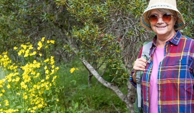 Senior vrouw die buiten in het bos loopt, dicht bij een groep gele bloemen