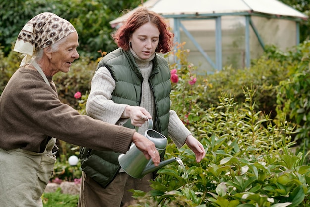 Senior vrouw die haar kleindochter uitlegt waar ze bloemen water moet geven