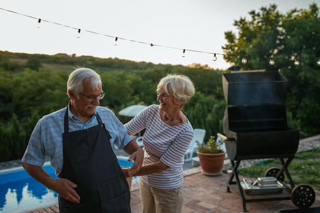 Senior vrouw die haar man helpt het schort te binden als hij gaat barbecueën in de achtertuin