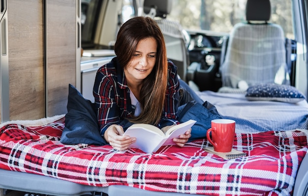 Senior vrouw die in een camper zit terwijl ze een boek leest en koffie drinkt - Focus op gezicht