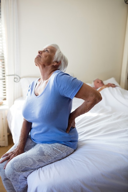 Senior vrouw die lijdt aan rugpijn in de slaapkamer thuis