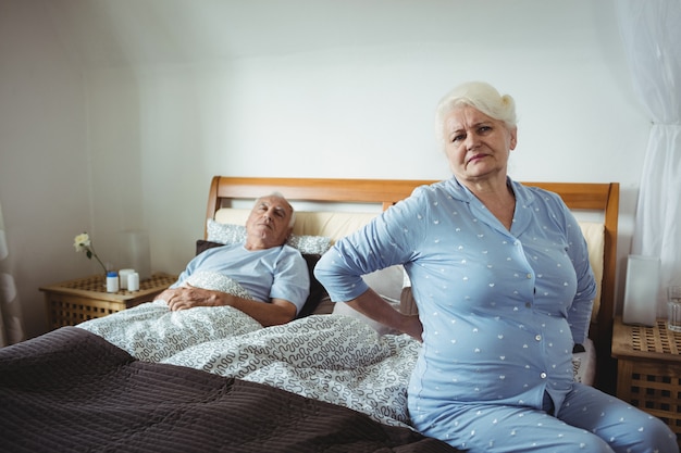 Senior vrouw die lijdt aan rugpijn zittend op bed