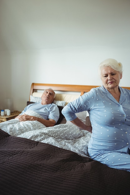 Senior vrouw die lijdt aan rugpijn zittend op bed