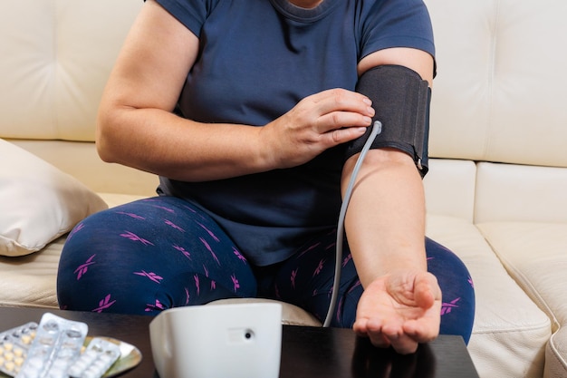 Senior vrouw die thuis de bloeddruk controleert oudere vrouw die lijdt aan hoge bloeddruk zittend op een bank en een pulsometer tonometer gebruikt