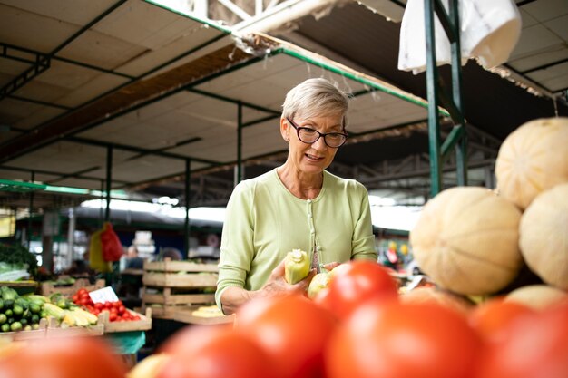 Senior vrouw die verse biologische groenten koopt op de markt en een tas vol gezond voedsel vasthoudt