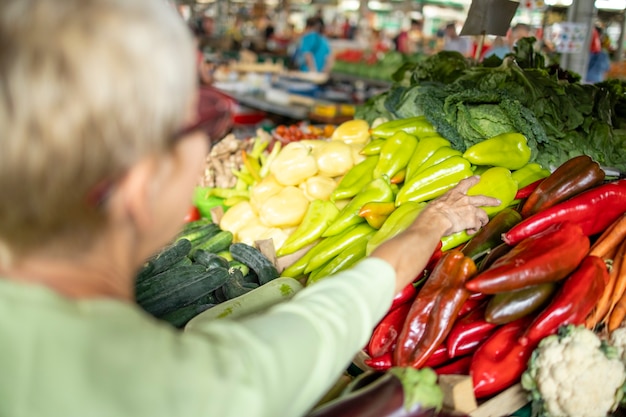 Senior vrouw die verse groenten en fruit koopt op de markt en een tas vol gezond voedsel vasthoudt