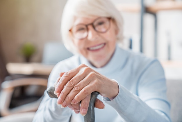 Senior vrouw die wandelstok vasthoudt terwijl ze thuis op de bank zit met focus op handen