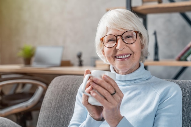 Senior vrouw die warme dranken drinkt die thuis op de bank zitten