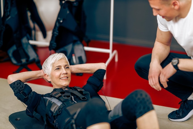 Foto senior vrouw doet sit-up oefeningen tijdens ems-training met personal trainer in de sportschool.