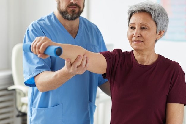 Senior vrouw haar hand uitrekken en training met dumbbels met arts permanent in de buurt en haar te helpen in het ziekenhuis