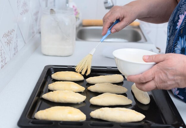 Senior vrouw handen borstelen rauwe taarten met ei voor het bakken op een bakplaat Selectieve aandacht Proces van het maken van taarten met appel vulling Koken thuis concept Traditie zelfgemaakte gerechten