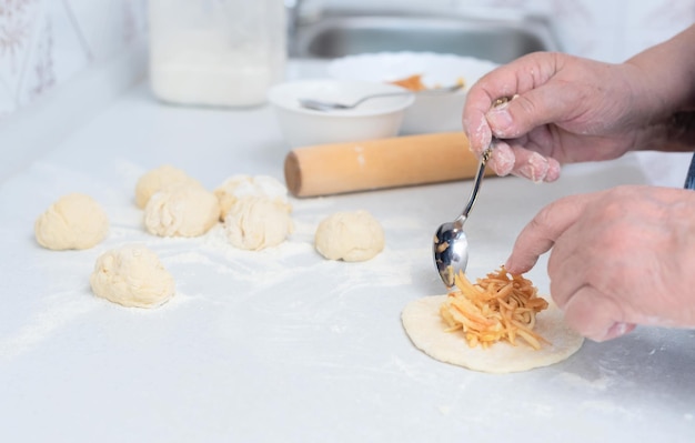 Senior vrouw handen zetten de appel vulling op het deeg voor taarten op een witte keukentafel Selectieve aandacht Proces van het maken van taarten met appel vulling Koken thuis concept Traditie zelfgemaakte gerechten