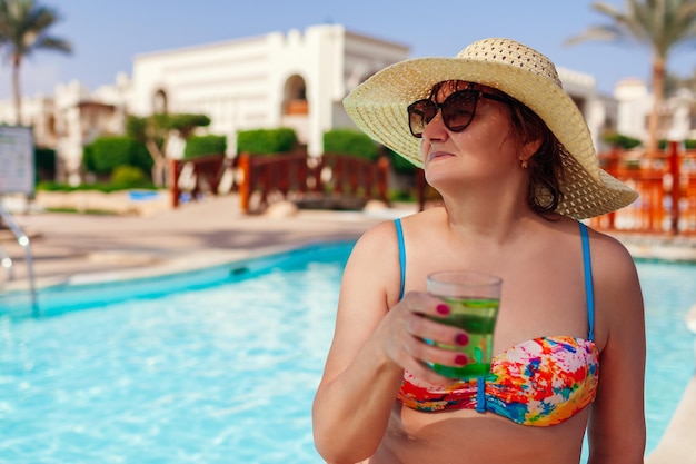 Senior vrouw in bikini drinkt cocktail in hotelzwembad Zomer tropische vakantie Exotisch resort met all inclusive