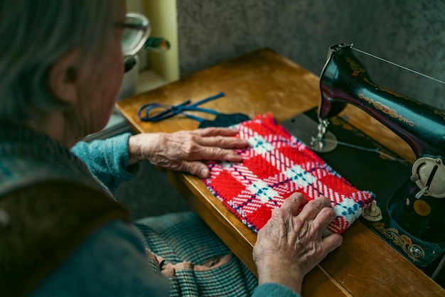 Senior vrouw in bril gebruik naaimachine gerimpelde handen van de oude naaisteroudere vrouw Oude naaimachine Klassieke retro-stijl handmatige naaimachine klaar voor naaiwerk