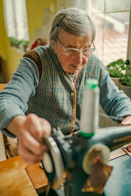 Senior vrouw in bril gebruik naaimachine gerimpelde handen van de oude naaisteroudere vrouw Oude naaimachine Klassieke retro-stijl handmatige naaimachine klaar voor naaiwerk