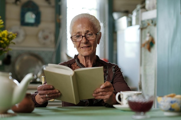 Senior vrouw in bril lezen boeiend verhaal of roman na het ontbijt