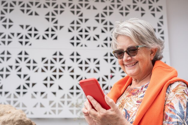 Senior vrouw in buitentuin glimlachend met behulp van draadloze technologie voor een bericht op mobiele telefoon, witte achtergrond