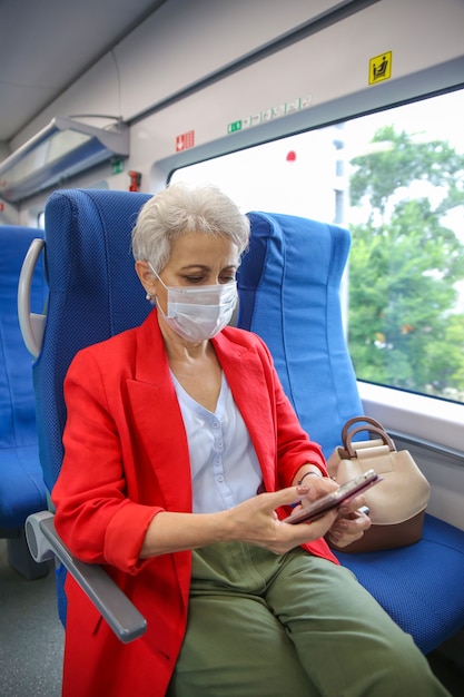Senior vrouw in een rood jasje en een medisch masker rijdt op een trein