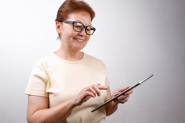 Senior vrouw in glazen gebruikt een tablet op wit in een licht T-shirt