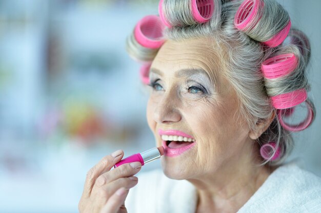 Senior vrouw in haarrollers met lippenstift thuis